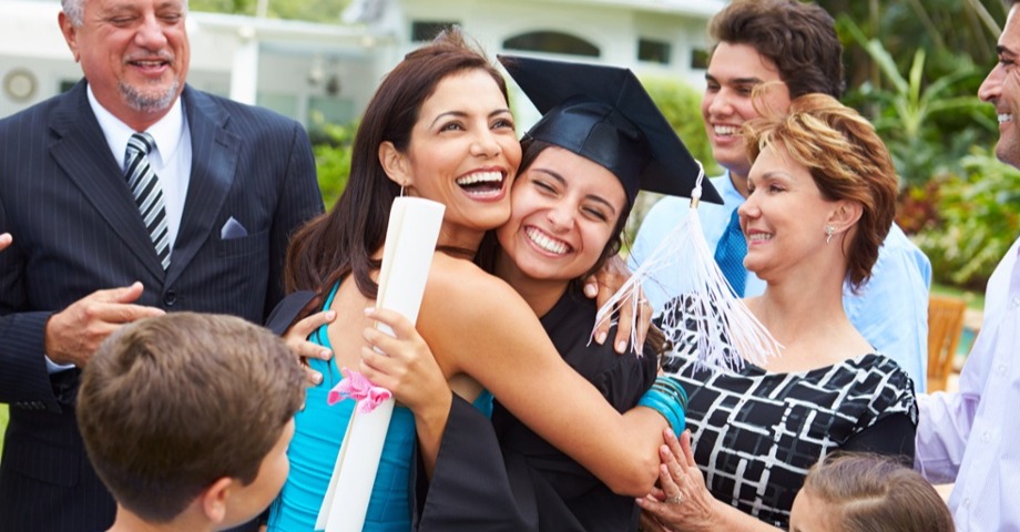 A woman hugging a girl in a graduation cap and gown. Both have wide smiles and seem very happy. 