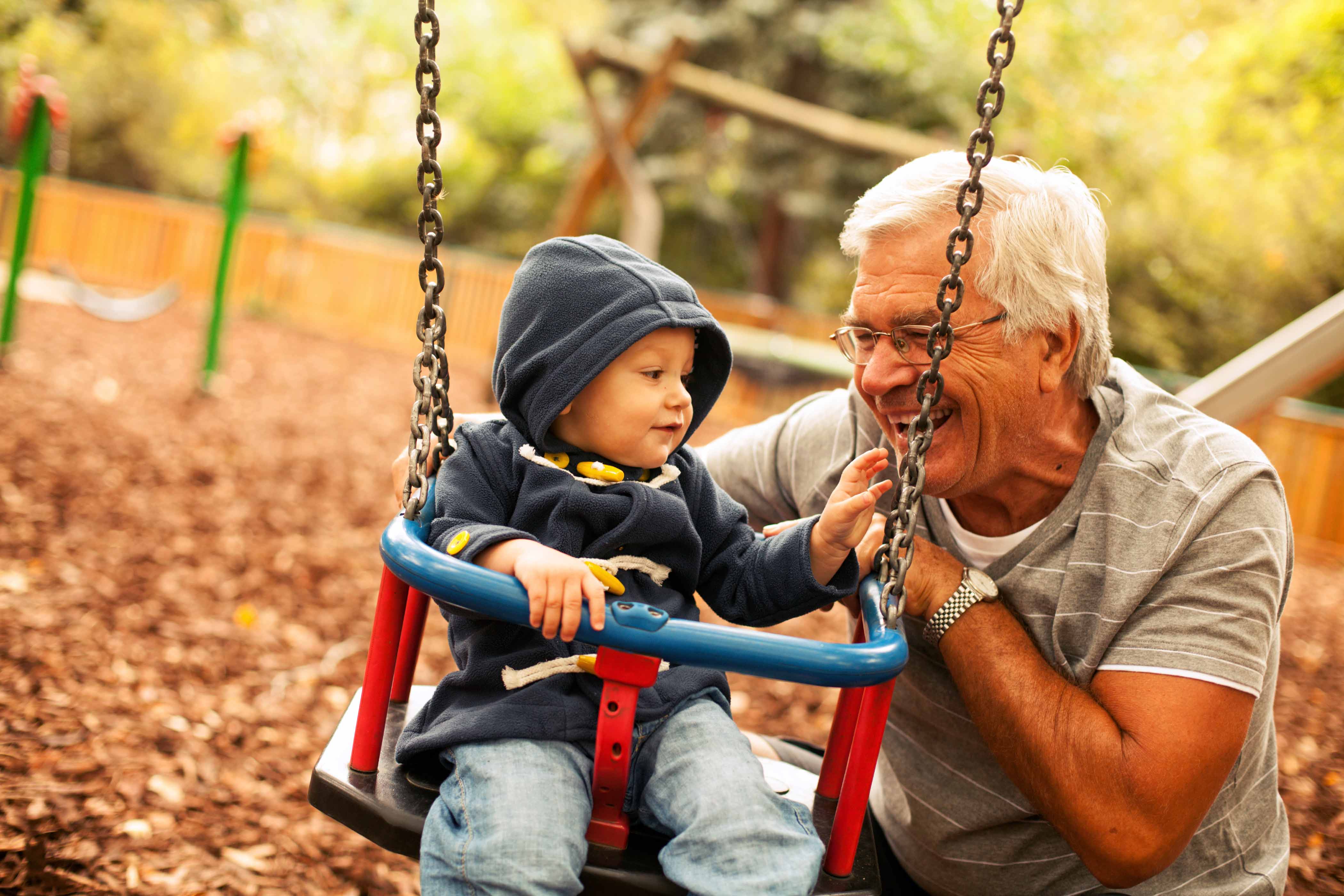Smiling grandpa pushing his grandchild in a swing 